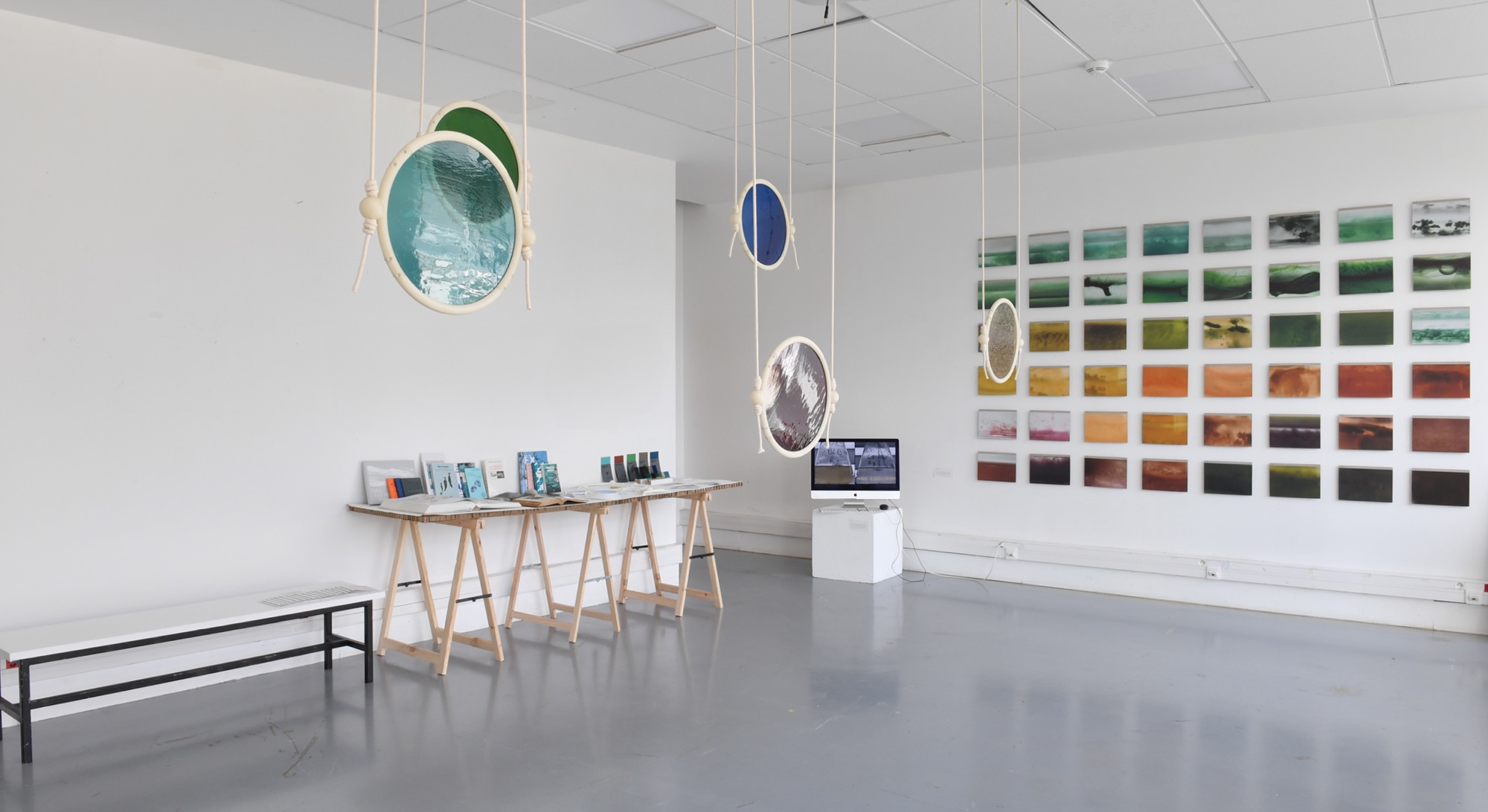 Vue de l’exposition : hublots suspendus et mur d’échantillons de couleurs d’eau